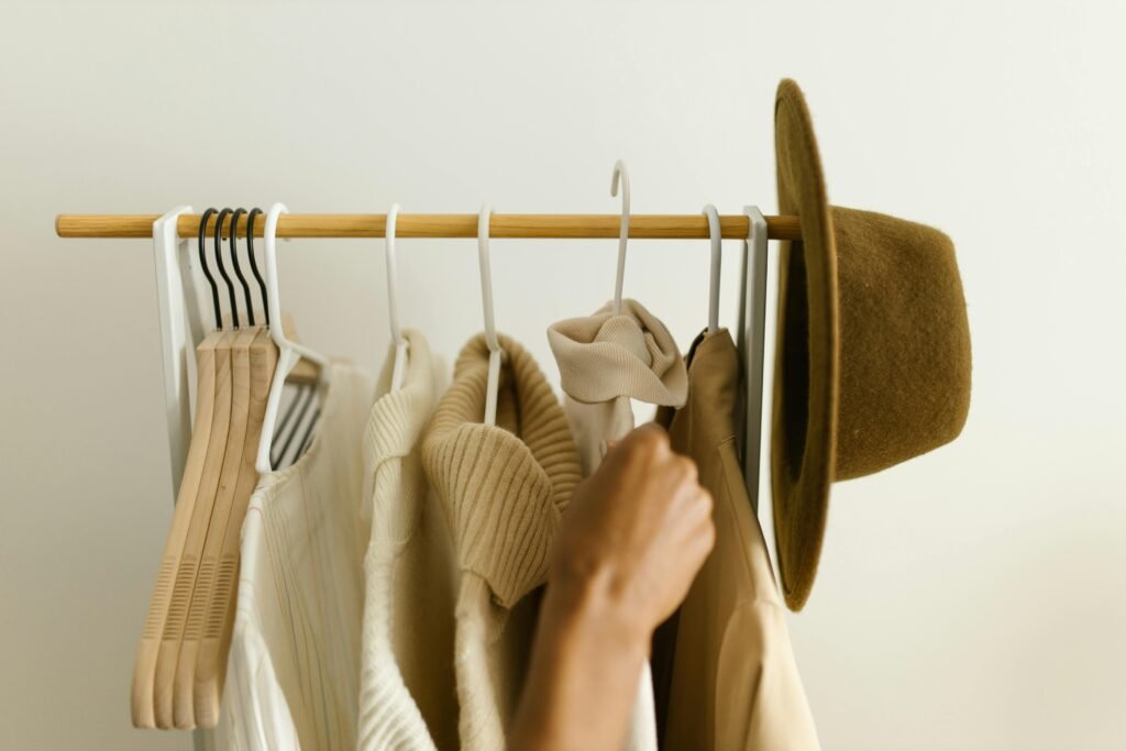 WARDROBE ESSENTIALS Stylish beige and brown clothes on a rack with a hand reaching in.